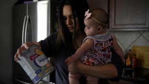 Une mère tenant dans ses bras sa fille de 5 mois verse le contenu d’un pot de lait maternisé dans le dernier pot de sa réserve, au Texas.