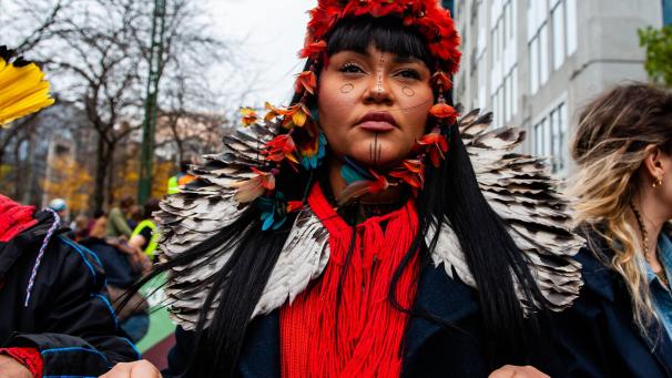 Une femme indigène est vue portant des plumes rouges et de la peinture traditionnelle sur son visage pendant la marche pour le climat.