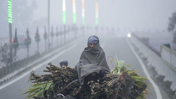 Un homme se couvre d'une couverture et monte sur une charrette à cheval par une matinée froide et brumeuse à Jammu, en Inde.