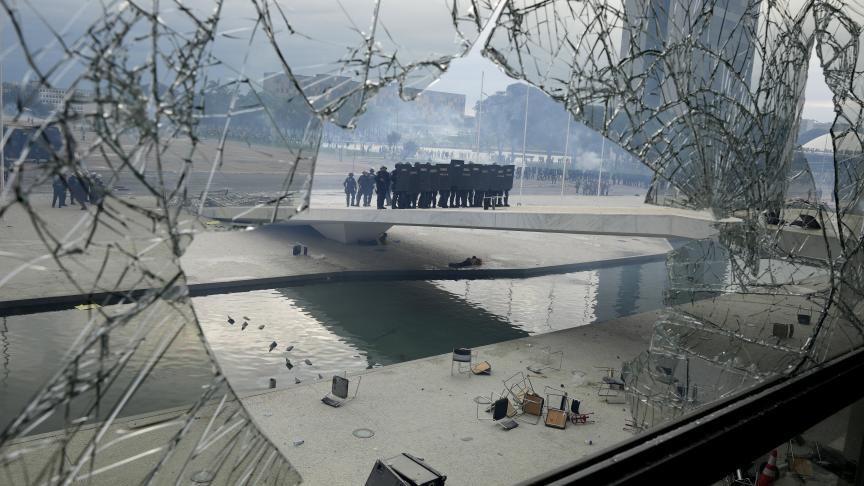 La police se tient de l'autre côté d'une fenêtre du palais du Planalto qui a été brisée par des manifestants, partisans de l'ancien président brésilien Jair Bolsonaro.